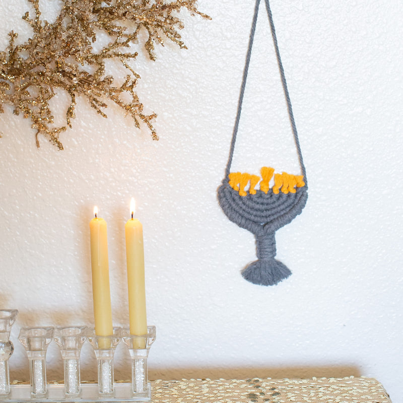 hanukkah wall decoration displayed in jet, a blue/grey color, on wall above lit candles near gold glittered foliage