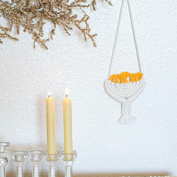 unique hanukkah decorations displayed in white on wall near lit candles and gold glittered foliage